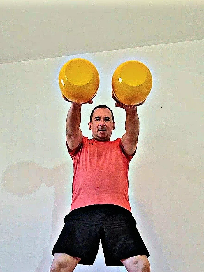 Daniel Bata hält zwei Kettlebells über dem Kopf