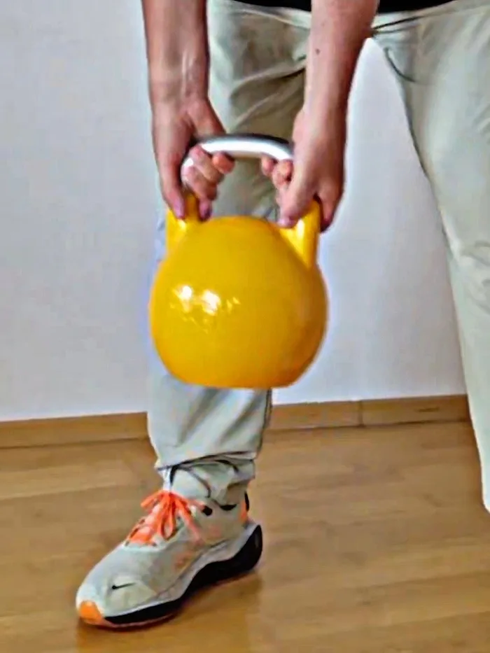Gelbe Kettlebell wird zwischen den Beinen gehalten