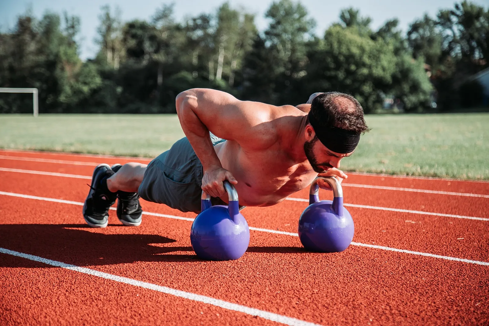 Sportler macht Liegestütze auf zwei Kettlebells auf einer Laufbahn